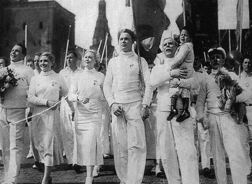Marion, her son, and Martinov proudly march with other Soviets garbed in white (Circus)